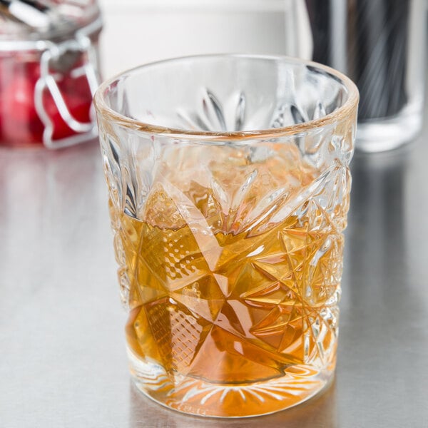 A Libbey Hobstar double old fashioned glass with brown liquid and ice.