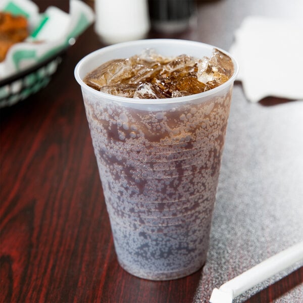 A Dart translucent plastic cup with ice and brown liquid and a straw on a table.