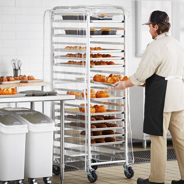 A full height bun and sheet pan rack with a clear cover, holding multiple trays of baked goods in a commercial kitchen setting.