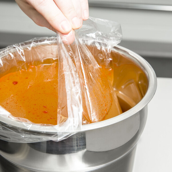 A hand using a 4 Qt. Round PTL Pan Liner to cover a bowl of soup.