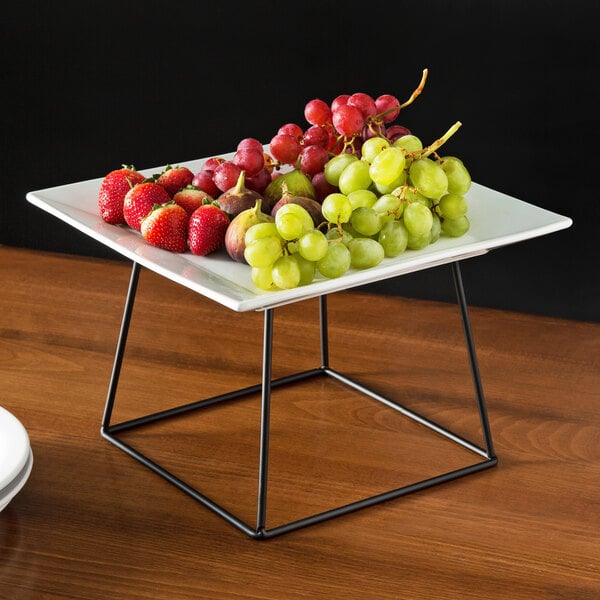 A table with an Acopa Square China plate of grapes and strawberries on a black display stand.