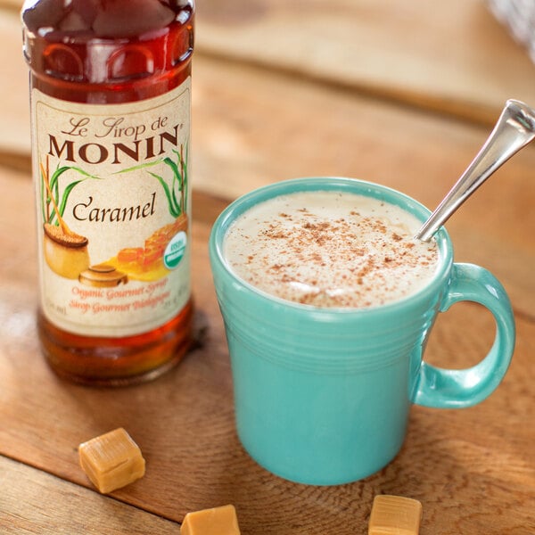 A blue mug of coffee with Monin Organic Caramel Flavoring Syrup and a spoon.