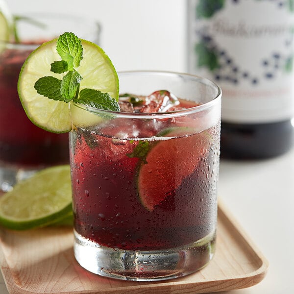 A glass of red Monin blackcurrant drink with a slice of lime and mint.