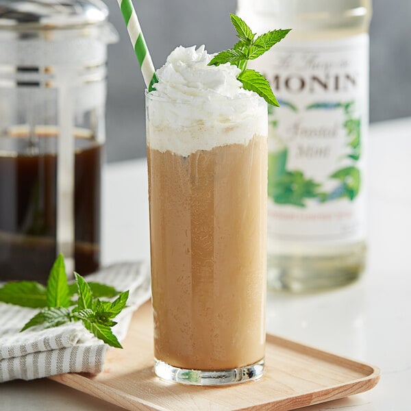 A glass of brown liquid with whipped cream and Monin Premium Frosted Mint syrup garnished with mint leaves.