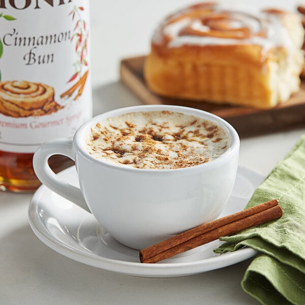 A cup of coffee with cinnamon sticks and Monin Cinnamon Bun flavoring on a table.