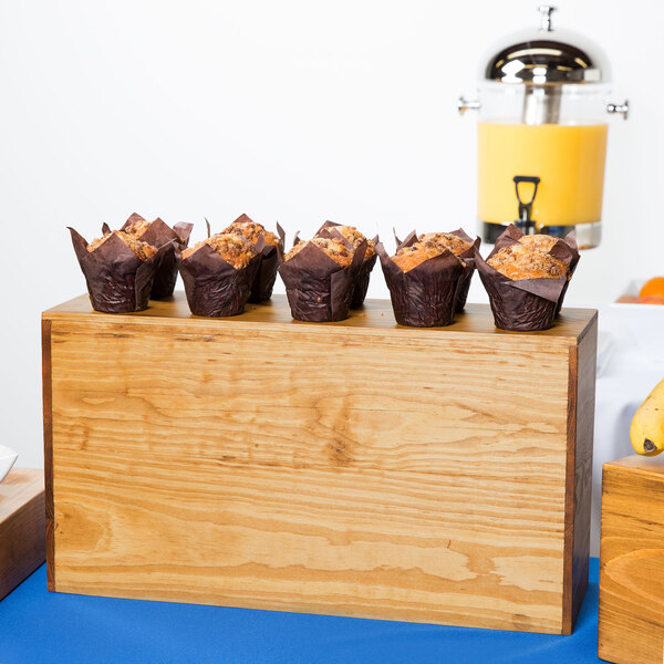 A Cal-Mil rustic pine rectangle plate riser holding a group of muffins on a table outdoors.