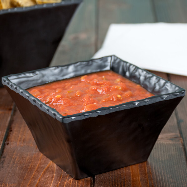 A black square bowl of salsa on a table with chips.
