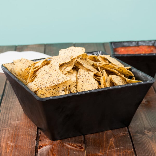 A black Cal-Mil faux slate square bowl filled with chips and salsa on a table.
