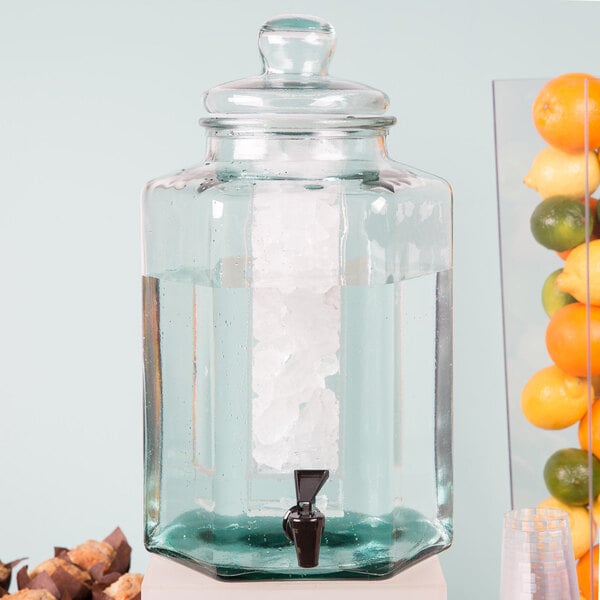 A Cal-Mil glass beverage dispenser with ice and fruit inside.