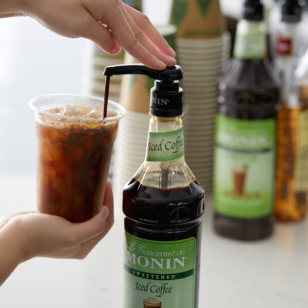 A person pouring Monin iced coffee concentrate into a plastic cup.