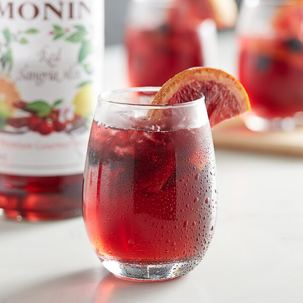 A glass of Monin red sangria with a slice of orange on the rim.