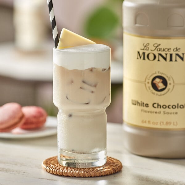 A glass of milkshake with a straw and Monin White Chocolate Flavoring Sauce on the side.