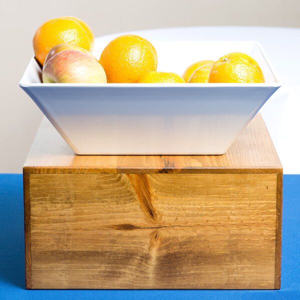 A bowl of oranges and apples on a Cal-Mil Madera rustic pine square riser.