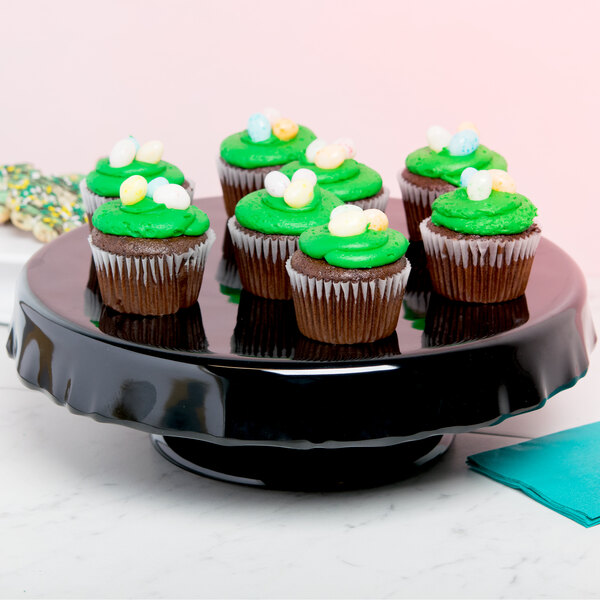 A black Elite Global Solutions ruffled edge melamine cake stand with a cupcake with green frosting and candy on top.