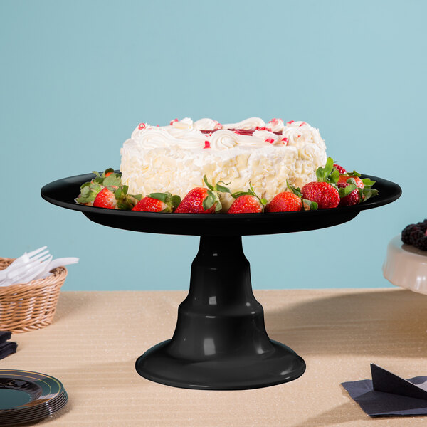 A black Elite Global Solutions plate stand holding a cake with strawberries on a table in a bakery.