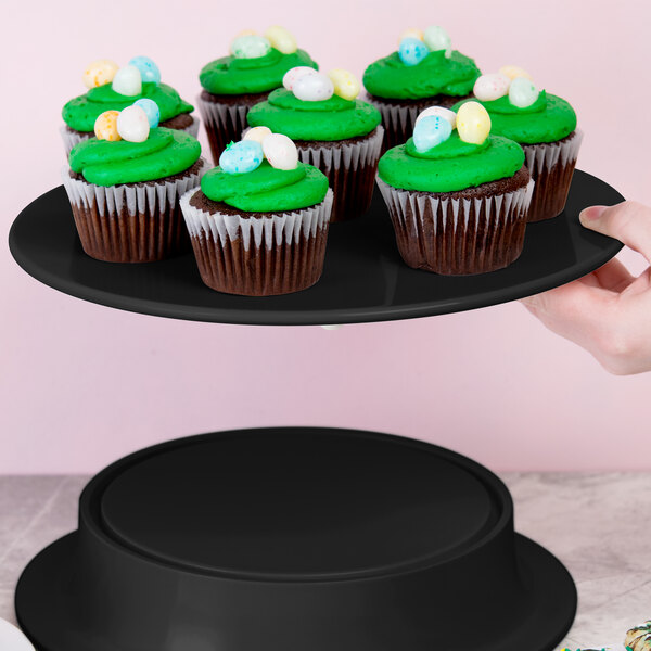 A person holding a black Elite Global Solutions melamine plate with cupcakes on it.