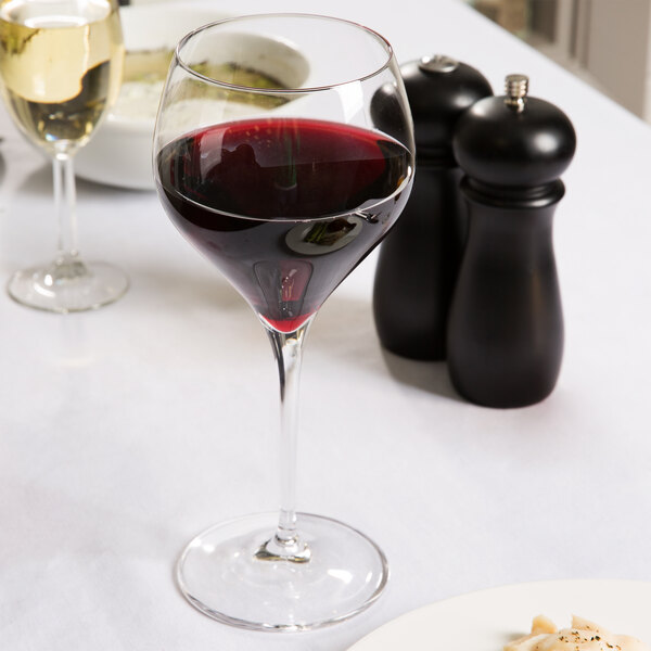 A close-up of a Spiegelau Adina Prestige burgundy wine glass filled with red wine on a table.