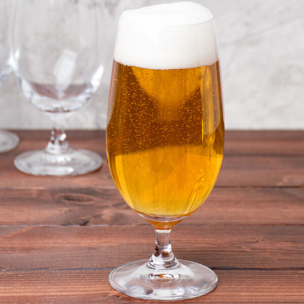 A Spiegelau stemmed Pilsner glass filled with yellow liquid on a table.
