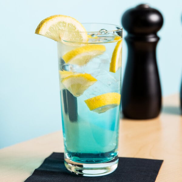 A clear Spiegelau Collins glass with blue liquid and a lemon wedge.