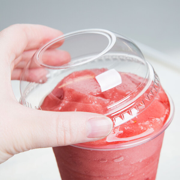 A hand using a Dart clear plastic dome lid on a plastic cup with a red smoothie inside.