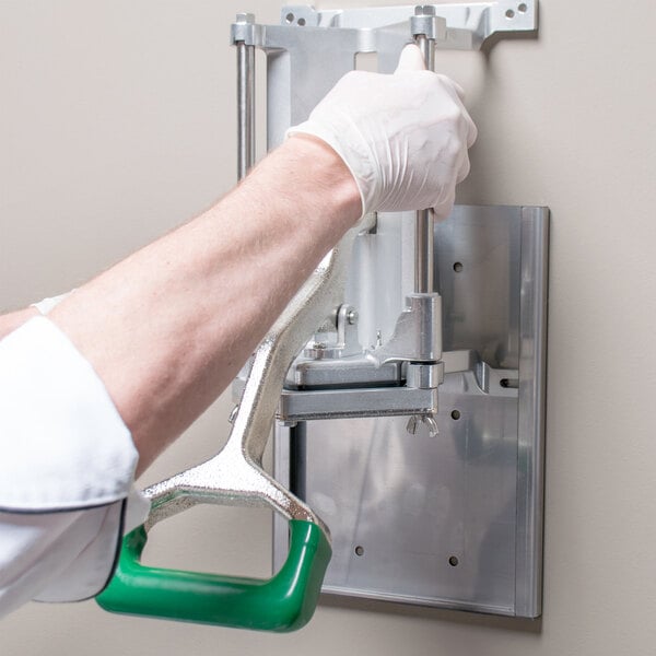 A person in white gloves using a green Garde French fry cutter on a metal wall bracket.