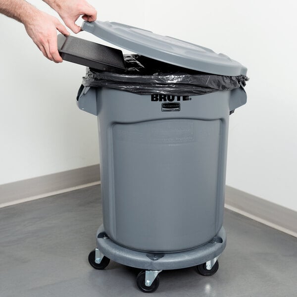 A person using a black Rubbermaid lid to put a white trash bag in a gray Rubbermaid trash can.