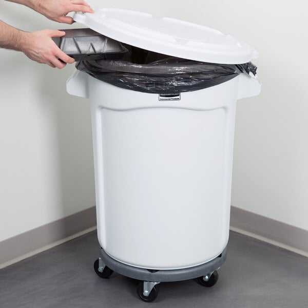 A person putting a trash bag into a Rubbermaid white trash can with white plastic lid on it.