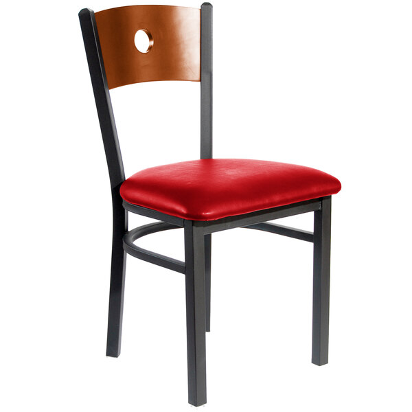 A BFM Seating metal side chair with a cherry wooden back and red vinyl seat.