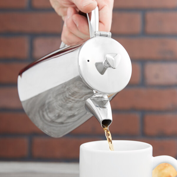 A hand pouring coffee from a Vollrath Triennium coffee pot into a white mug.
