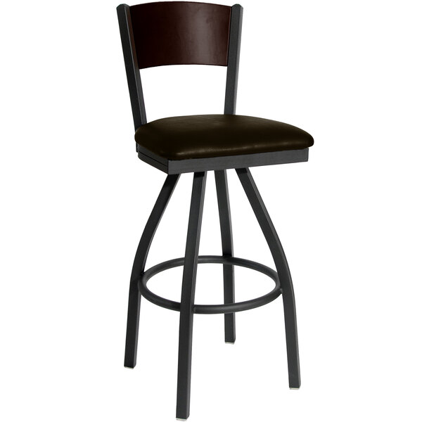 A BFM Seating black metal swivel bar stool with a walnut finish wooden back and dark brown vinyl seat.