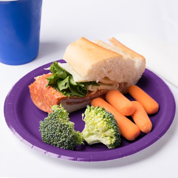 A Creative Converting amethyst purple paper plate with a sandwich, carrots, and broccoli on it.