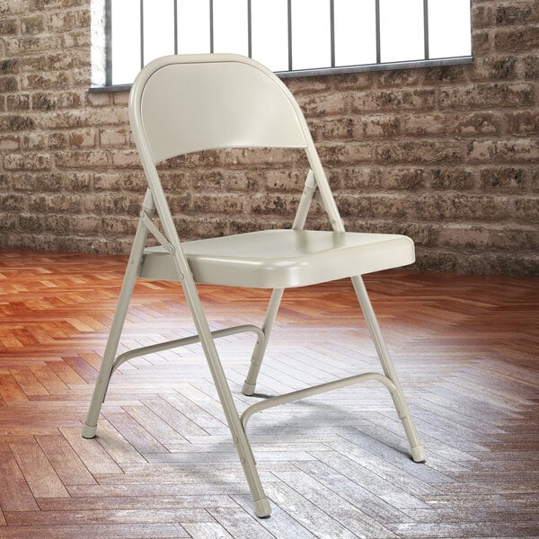 A National Public Seating gray metal folding chair in front of a brick wall.