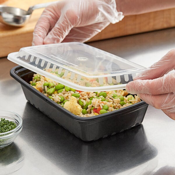 A person in gloves using a plastic lid to cover a rectangular food container.