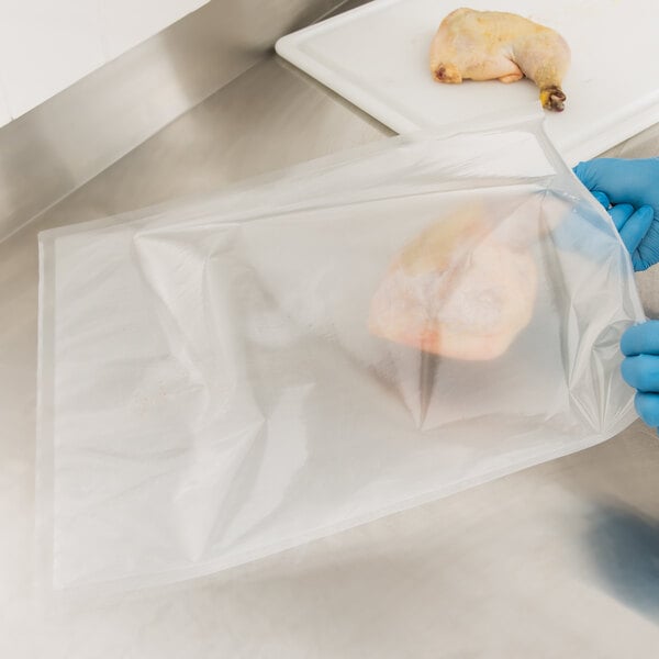 A person in blue gloves using an ARY VacMaster 2 gallon mesh vacuum packaging bag to package a chicken leg.