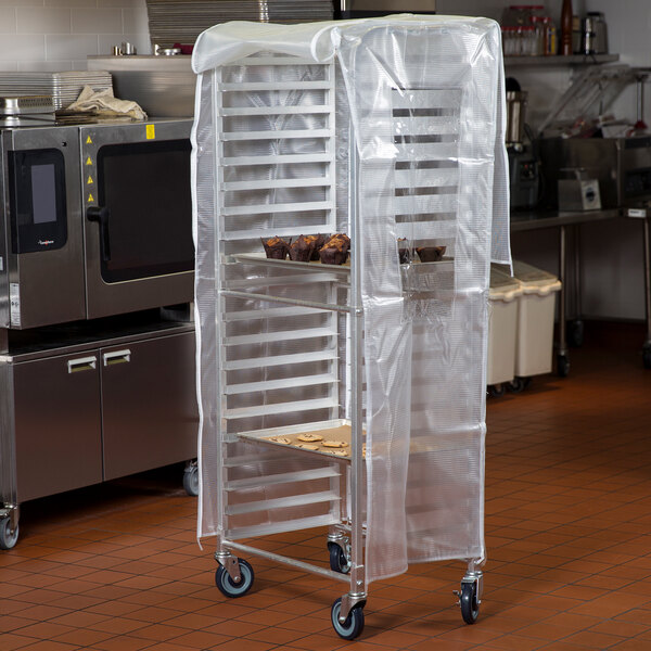 A translucent plastic bun pan rack cover placed over a tall metal rack in a commercial kitchen.