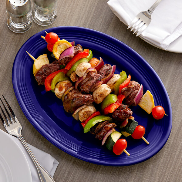 A Tuxton cobalt oval china platter with skewered meat and vegetables on a table.