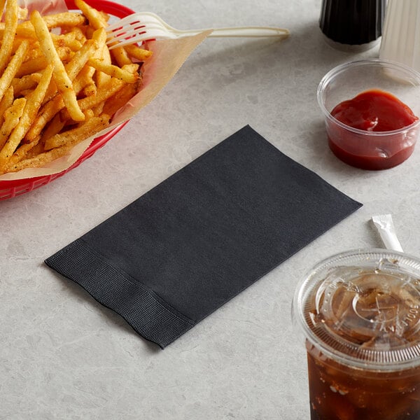 A basket of french fries and a black napkin with a white edge next to a drink.