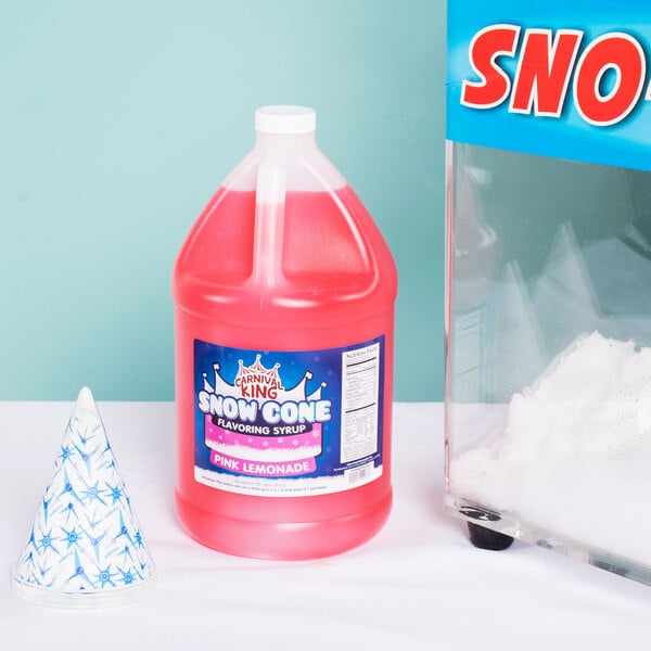 A large jug of pink Carnival King Pink Lemonade Snow Cone Syrup with a pink liquid next to a container of snow.