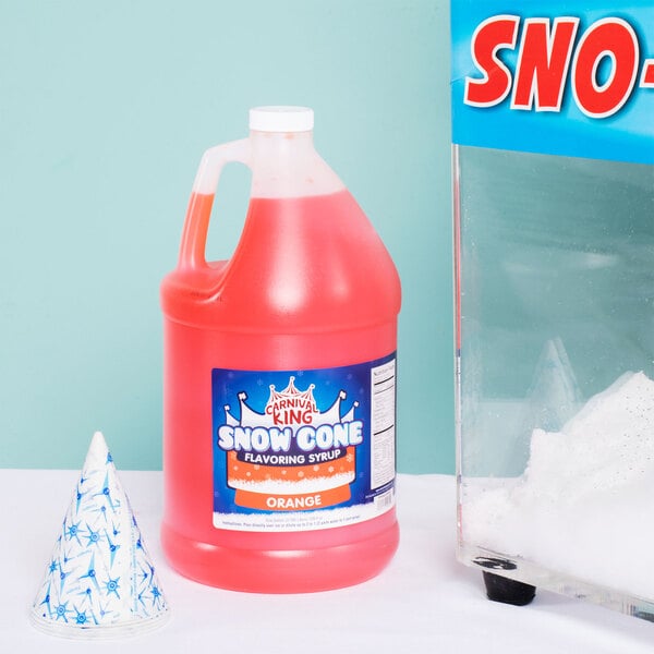 A large plastic jug of Carnival King Orange Snow Cone Syrup next to a snow cone and a bottle of snow.