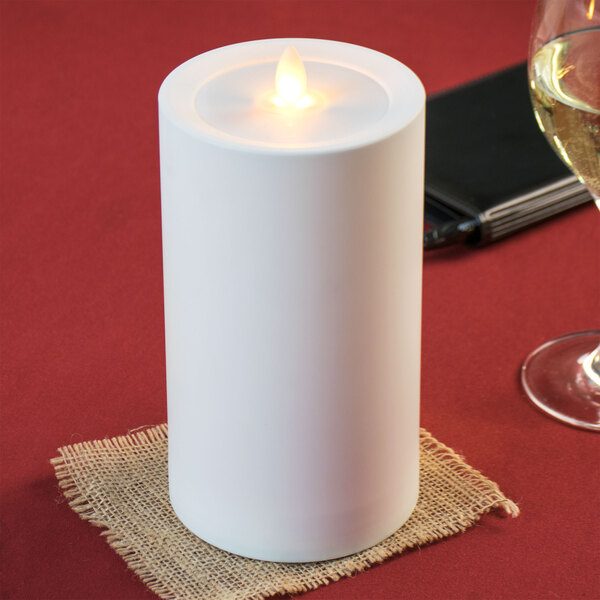 A white Sterno Mirage flameless LED candle on a burlap napkin next to a glass of wine.