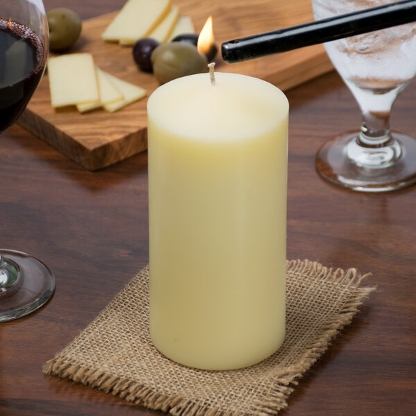 A white Sterno Ivory wax pillar candle on a table with a lighter and wine.