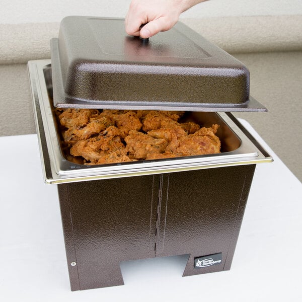 A person using a Sterno Copper Vein chafer to put food into a metal pan on a table.
