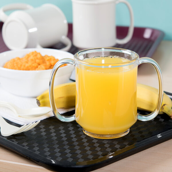 A tray with a clear Tritan plastic mug filled with orange juice and a banana on a table in a hospital cafeteria.