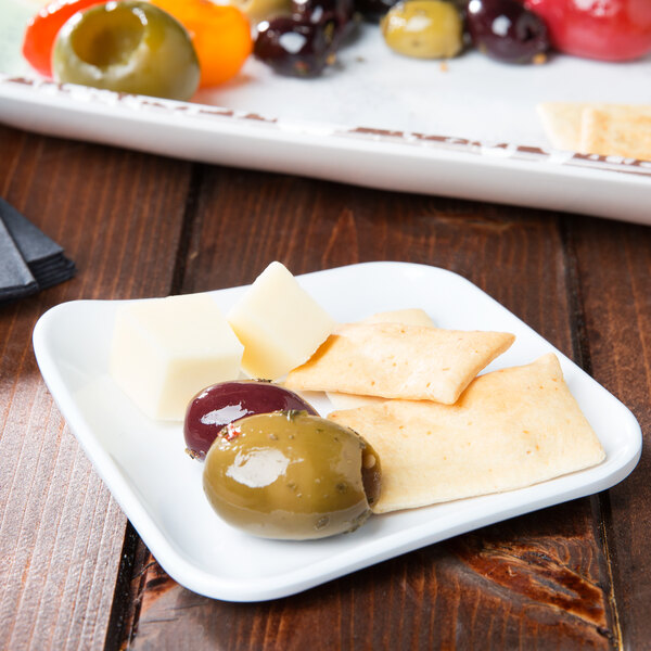 A white square melamine plate with cheese, crackers, and olives on it.