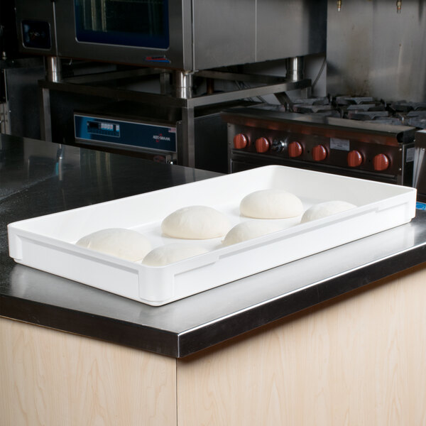 A white MFG Tray fiberglass dough proofing box on a counter full of dough.