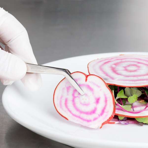 A person using Mercer Culinary curved precision tongs to plate radishes.