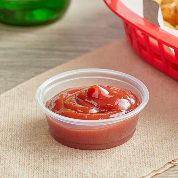 A clear plastic Choice portion cup filled with ketchup on a table.