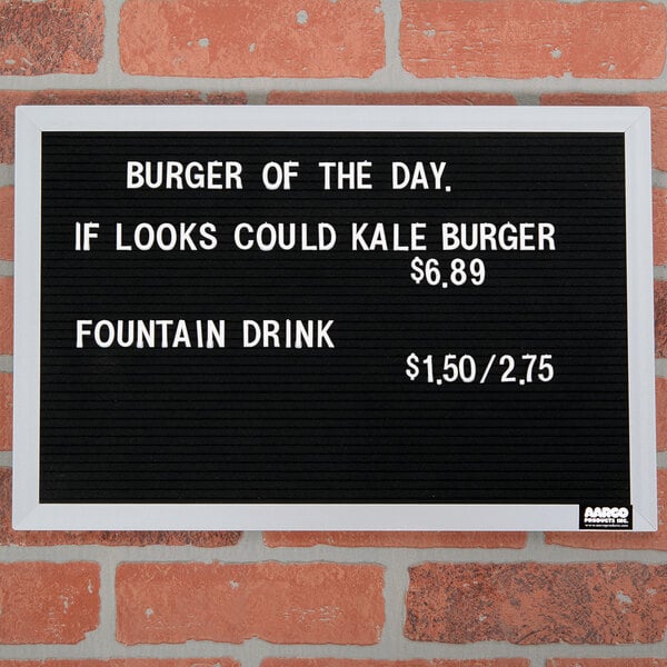 A black Aarco felt message board with white text reading "Burger of the Day" on a brick wall above a counter.