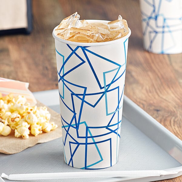 A white paper cup with a blue and white cylindrical container with blue lines filled with ice tea and popcorn.