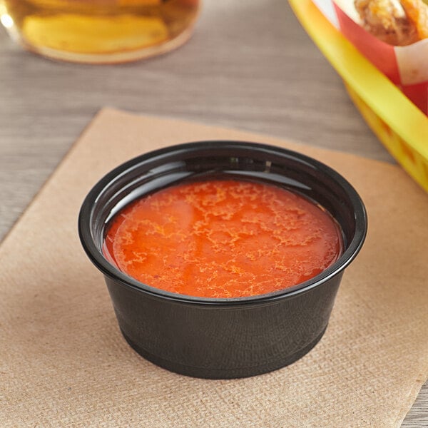 A Choice black plastic souffle cup filled with red sauce.